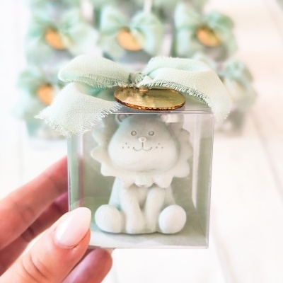 Pequena figura de leão branco numa caixa transparente com laço verde e medalha dourada