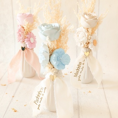 Três mini vasos decorativos com flores artificiais em tons pastel e fitas com texto em português.