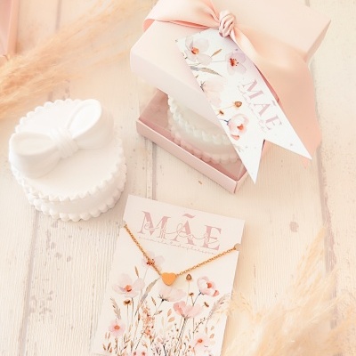 Colar dourado coração com embalagem de oferta rosa e cartão MÃE em superfície clara