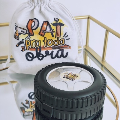 Saco de pano branco com frase e caixa redonda preta estilo pneu com frase, sobre superfície espelhada