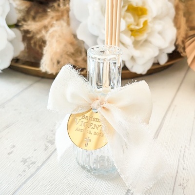 Difusor de fragrância com laço branco e etiqueta dourada em superfície de madeira clara