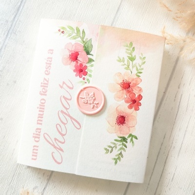 Caixa branca decorada com flores e texto em rosa sobre superfície de madeira clara