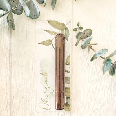 Vela castiçal castanha em embalagem transparente com papel decorativo de folhas verdes e texto 'bless you'