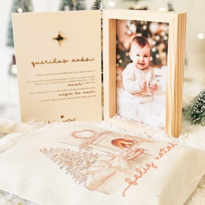 Moldura de madeira com fotografia de bebé, cartão com texto, saco de tecido branco com desenho e frase de Natal.
