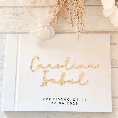 Livro branco com texto dourado e preto, decorado com flores secas sobre madeira clara