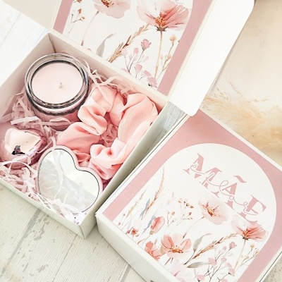 Caixa presente com vela, elástico de cabelo rosa, coração metálico e sino, com design floral rosa e branco.
