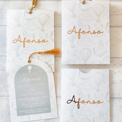 Convites de batizado em cartão branco com padrão cinza e nome Afonso em dourado com tassel.