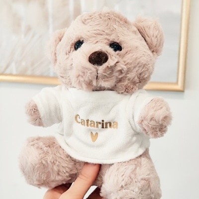 Ursinho de peluche bege com t-shirt branca e texto Catarina