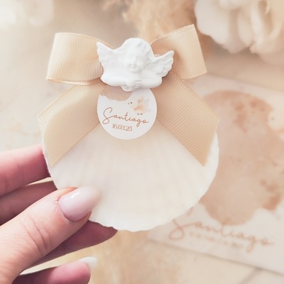 Concha marinha decorada com laço bege, anjo branco e etiqueta 'Santiago 16 03 25'