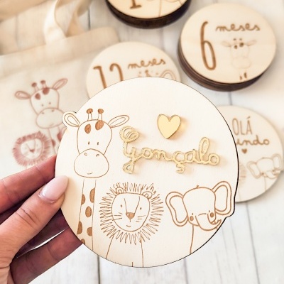 Discos de madeira com ilustrações de animais e textos em português para marcar meses de bebé.
