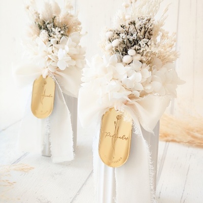 Duas velas decorativas brancas com flores secas e rótulos dourados