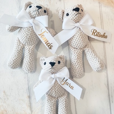 Três ursinhos de tecido bege claro com etiquetas de nomes e laços brancos