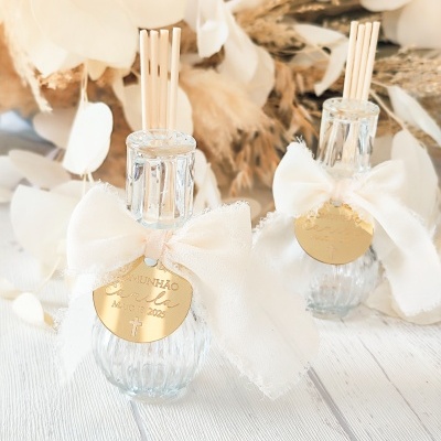 Dois difusores de ambiente em vidro transparente com laços brancos e medalhas douradas