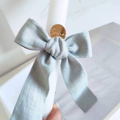 Vela branca com laço azul e etiqueta dourada em caixa com texto