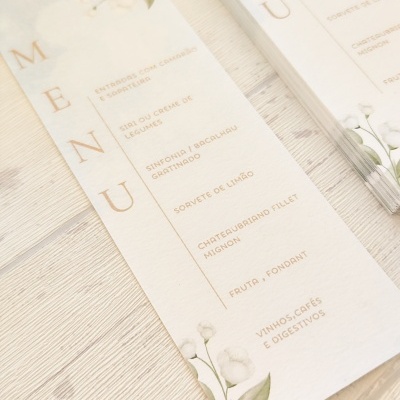 Menus em papel branco com ilustração floral sobre mesa clara.