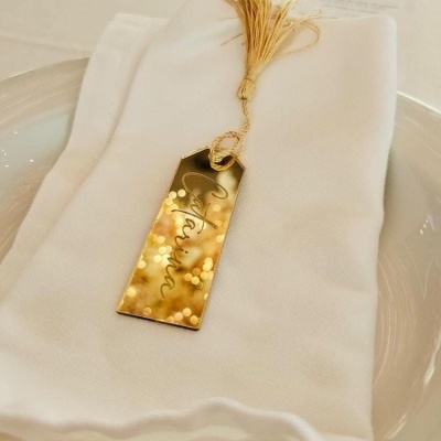 Marcador de mesa dourado com cacho dourado e nome Verónica sobre guardanapo branco em prato branco