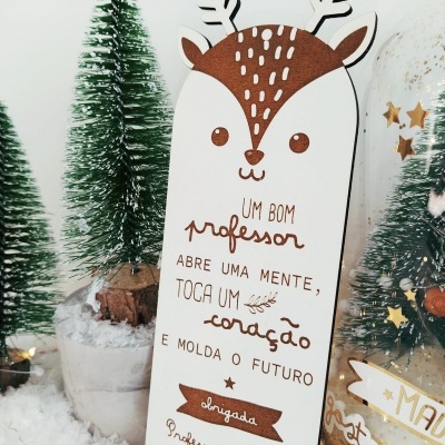 Placa decorativa de rena com texto para professora entre árvores e neve artificial