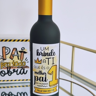 Garrafa com rótulo colorido e tampa dourada sobre superfície de vidro com placa decorativa ao fundo