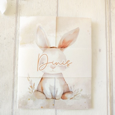 Cartão com desenho de coelho e nome Dinis vez sobre fundo de madeira clara