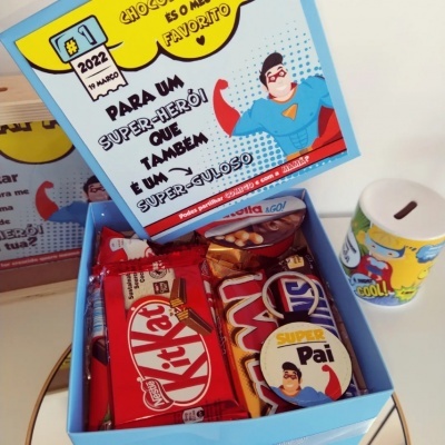 Caixa azul com chocolates Kit Kat, Twix e cookie, cartão com mensagem e cofrinho amarelo e branco