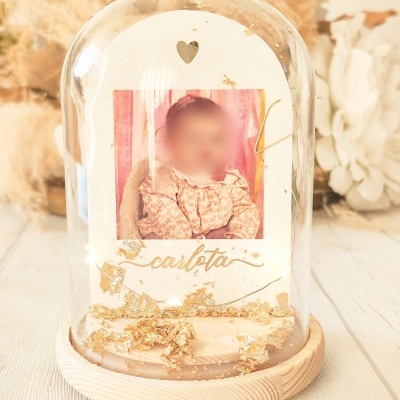 Objeto decorativo com foto de criança, base de madeira e cúpula de vidro com decoração dourada