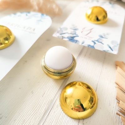 Bálsamo labial em embalagem dourada com cartão floral azul