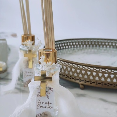 Difusores de ambiente com cruz dourada e tecido branco em superfície de mármore