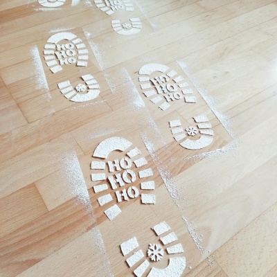 Pegadas de bota com texto HO HO HO e floco de neve em pó branco sobre chão de madeira