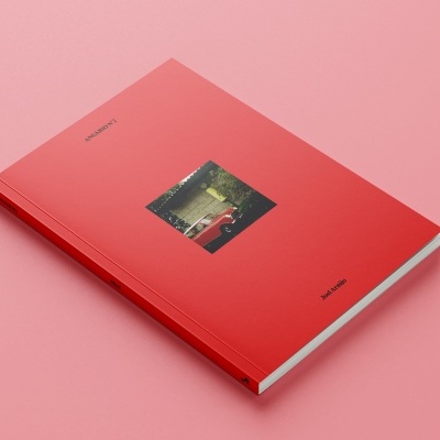 Livro vermelho com fotografia de carro na capa sobre superfície rosa