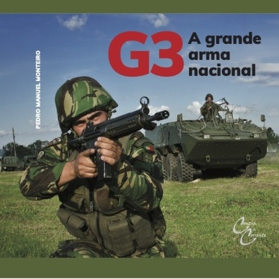 Soldado com espingarda G3 em uniforme camuflado diante de veículo militar blindado verde em campo aberto