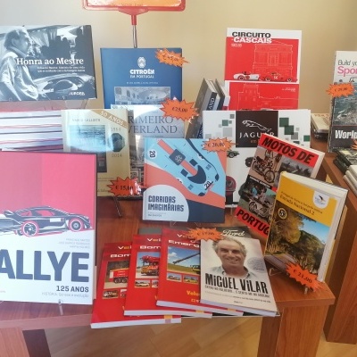 Livros e revistas sobre automóveis e corridas expostos numa mesa de madeira