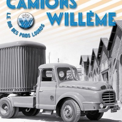 Camião antigo cinzento com texto promocional azul e armazéns ao fundo