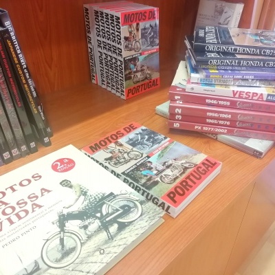 Livros sobre motociclos em estante de madeira, incluindo títulos em português