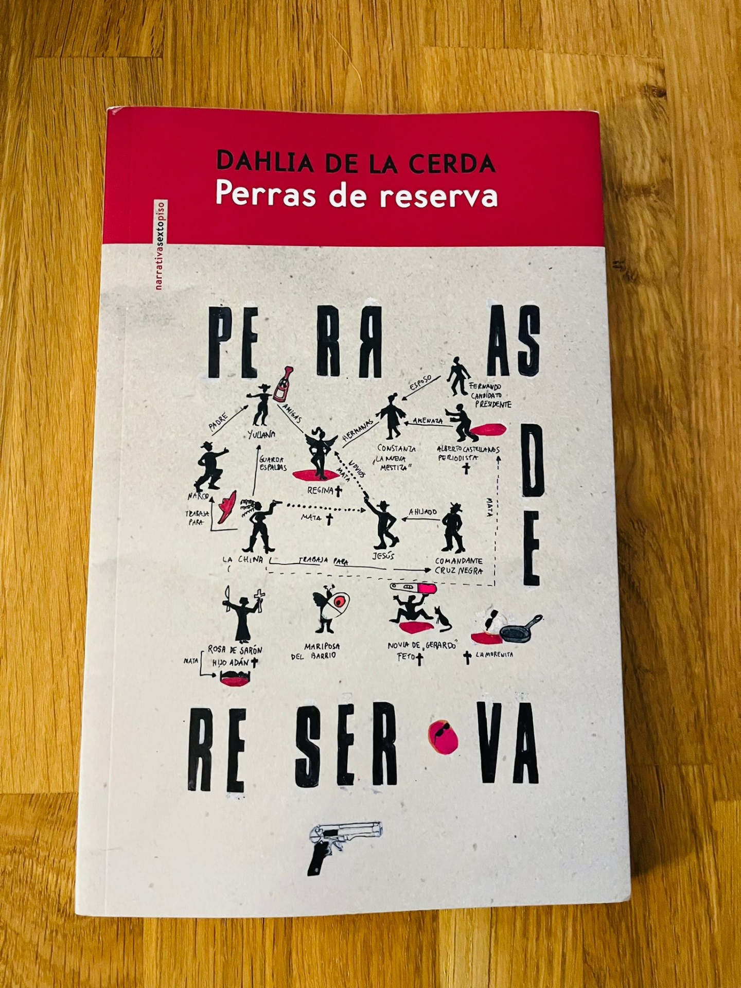 Perras de reserva, de Dahlia de la Cerda Capa de livro vermelho e branco com texto e ilustrações pequenas em preto e vermelho sobre mesa de madeira