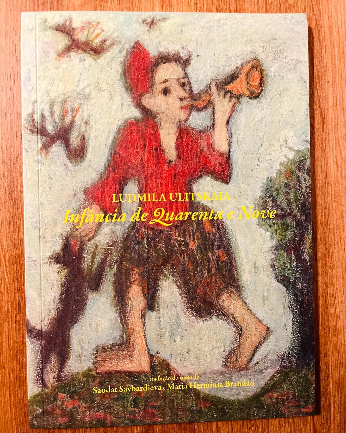Infância de Quarenta e Nove, de Ludmila Ulitskaia Capa de livro com figura infantil vermelha, tocando cornetinha, e gato preto