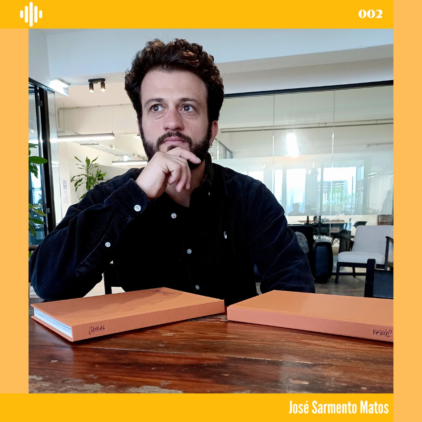 Homem sentado à mesa com dois cadernos castanhos em ambiente interior moderno