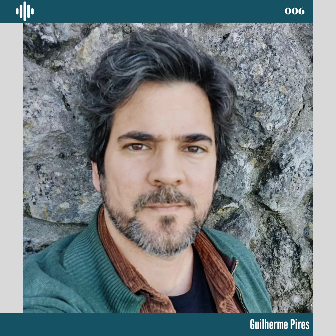 Homem com camisola verde e camisa castanha diante de parede de pedra com texto 'Guilherme Pires' e '006'