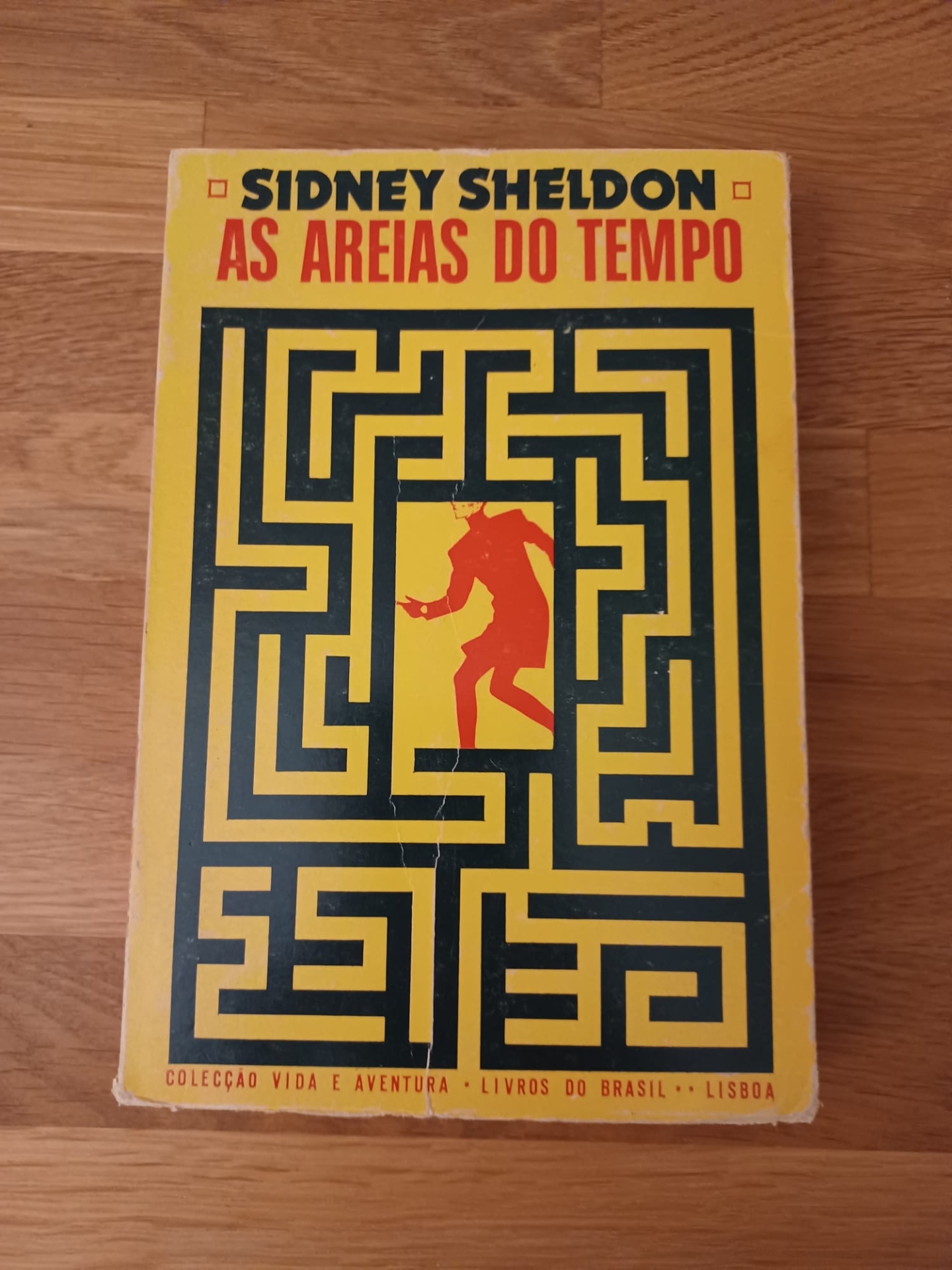 As Areias do Tempo, de Sidney Sheldon Capa do livro 'As Areias do Tempo' de Sidney Sheldon com labirinto amarelo e preto e figura vermelha