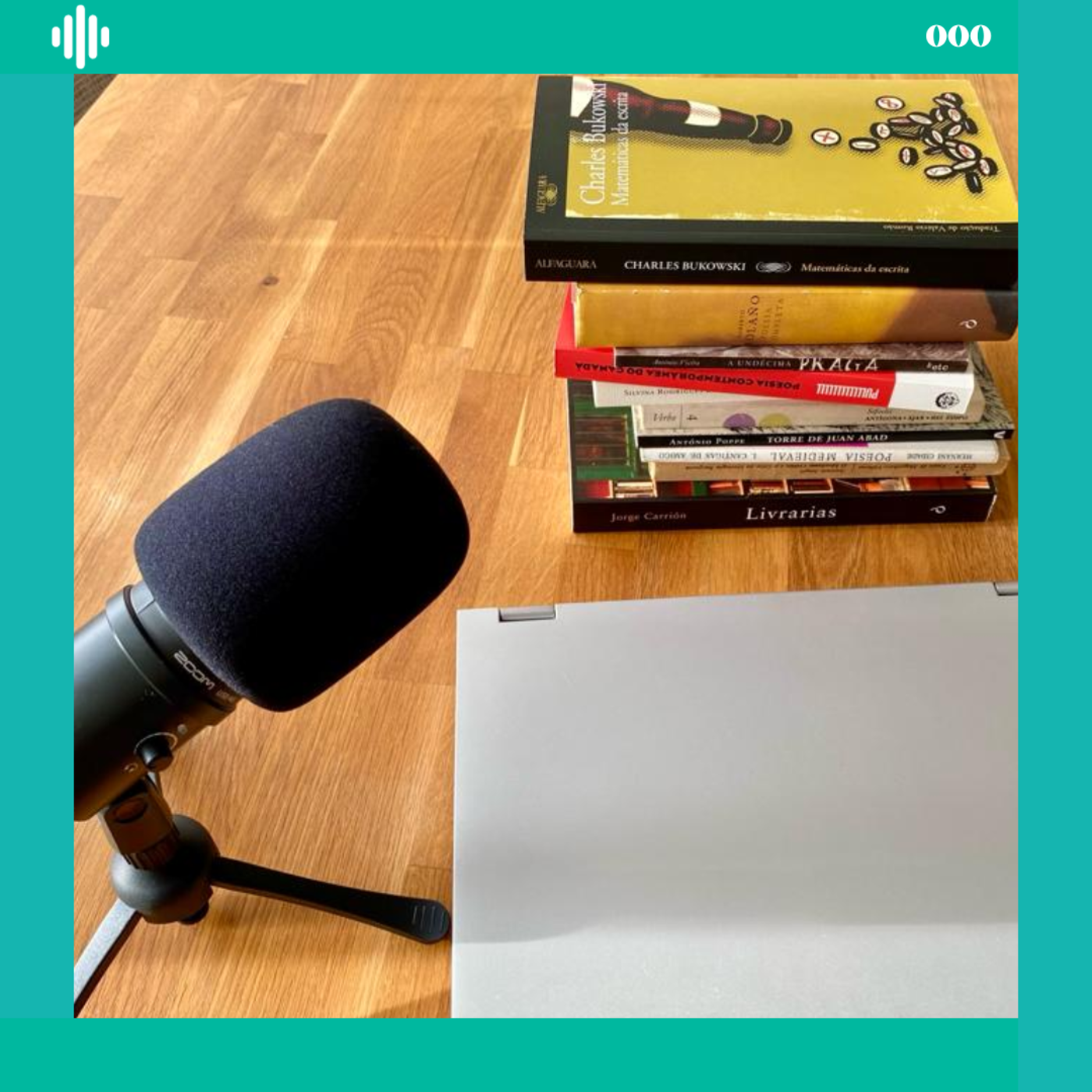 Microfone preto e portátil prateado ao lado de pilha de livros em mesa de madeira