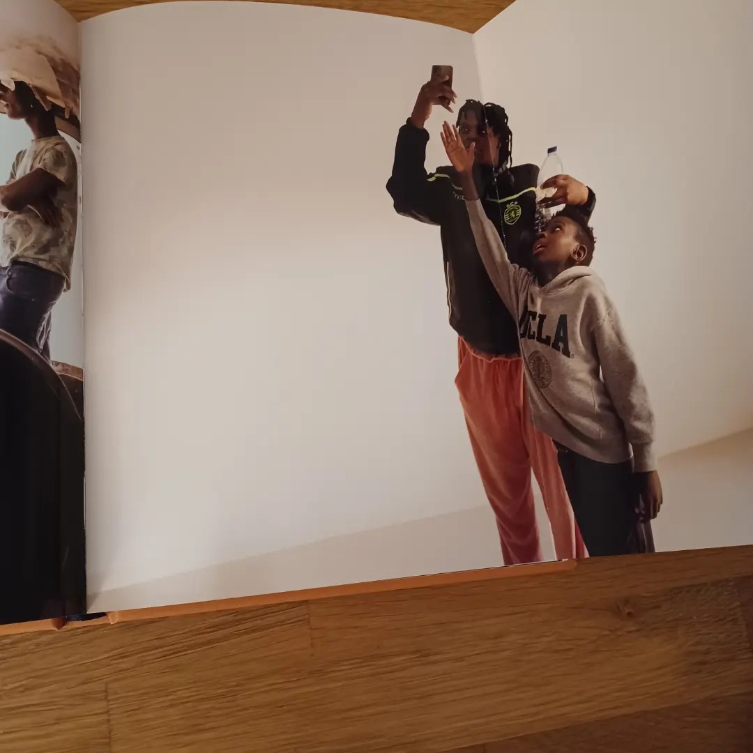 Jamaika, de José Sarmento Matos Pessoas a tirar selfie, página de livro aberta sobre chão de madeira