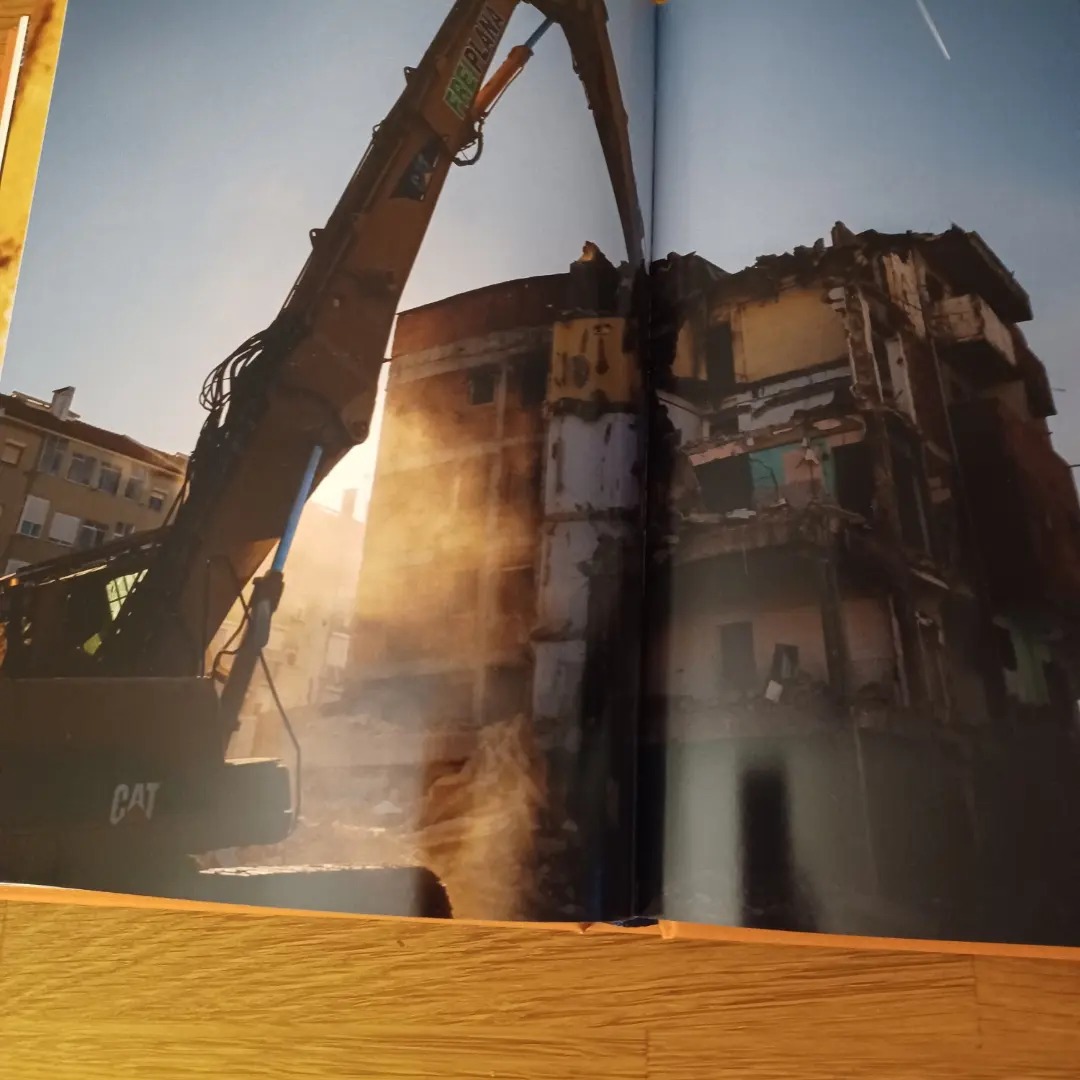 Jamaika, de José Sarmento Matos Escavadora CAT demole edifício amarelo e branco com luz solar intensa