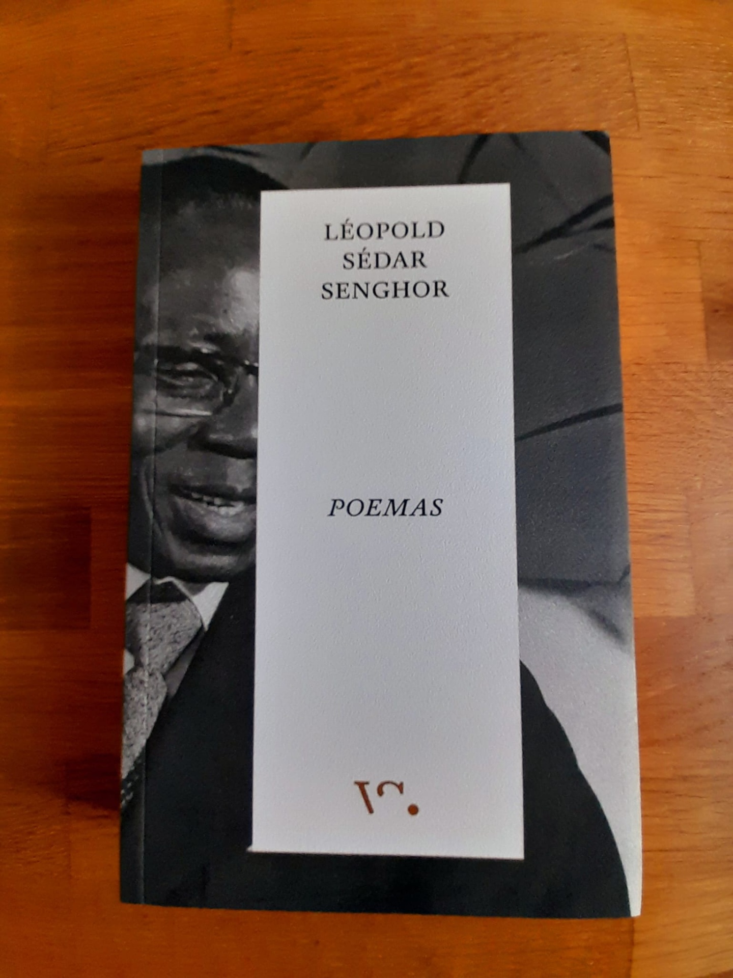 Poemas, de Léopold Sédar Senghor Livro Poemas de Léopold Sédar Senghor com capa preta e branca sobre mesa de madeira.
