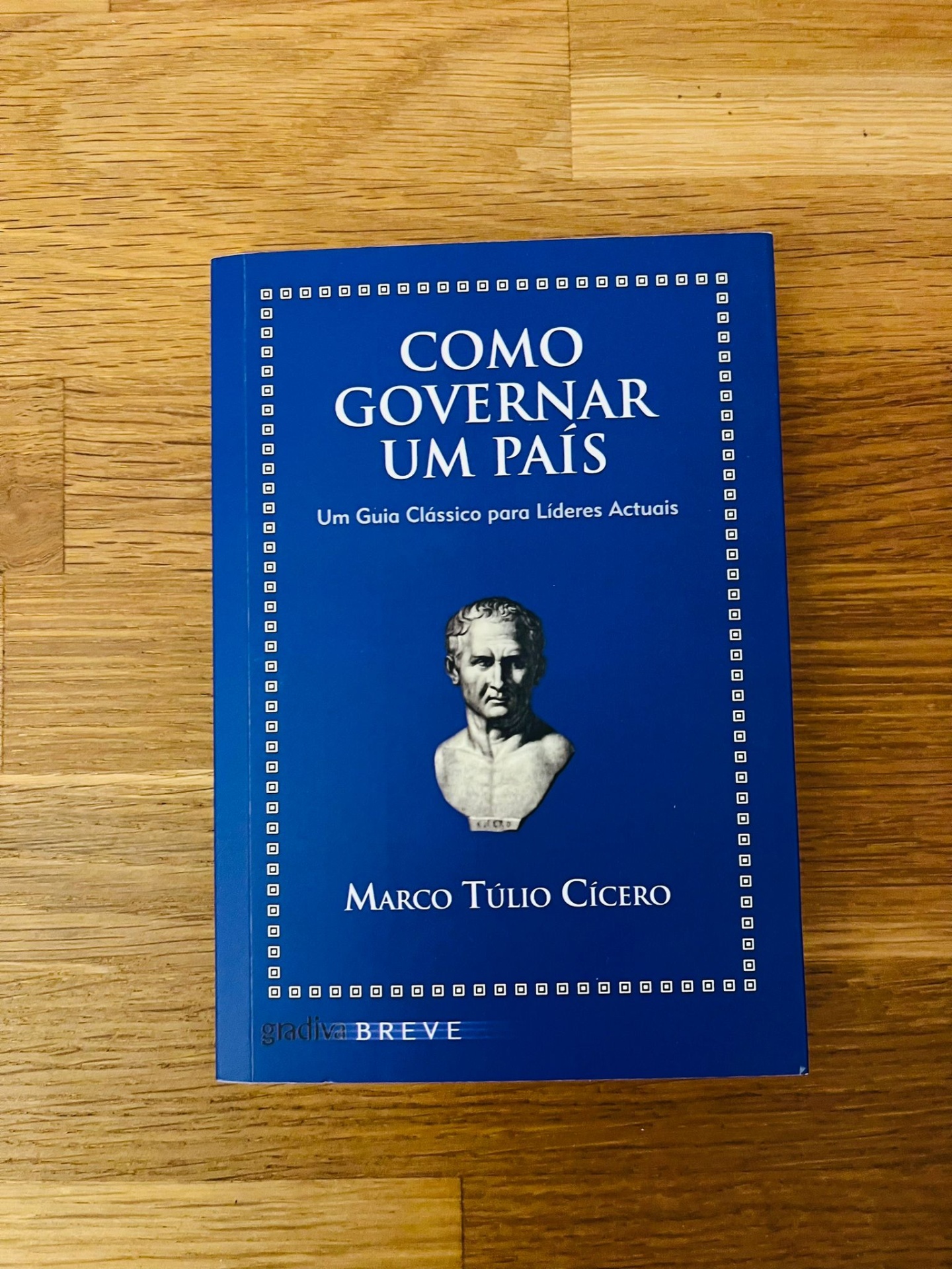 Como Governar um País, de Marco Túlio Cícero Livro azul 'Como Governar um País' com busto branco, sobre mesa de madeira clara
