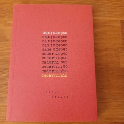 Livro de capa vermelha com texto e superfície de madeira clara ao fundo