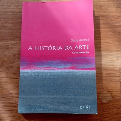 Livro 'A HISTÓRIA DA ARTE' de Dana Arnold com capa em rosa, cinza e azul sobre madeira clara