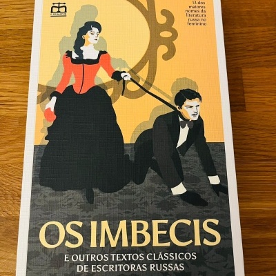 Livro com capa ilustrada mostrando mulher com vestido vermelho a segurar trela amarrada a homem com roupa preta