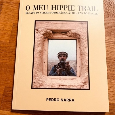 Capa de livro branco com título e fotografia de homem com câmara em abertura de parede areia
