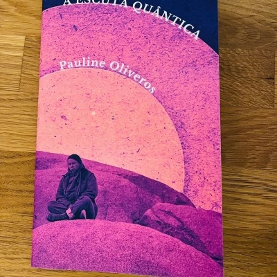 Capa do livro A Escuta Quântica de Pauline Oliveros com imagem de pessoa sentada sobre rochas em tons rosa e roxo.