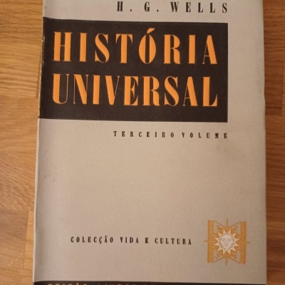Livro HISTÓRIA UNIVERSAL de H.G. Wells com capa cinza e letras em preto e laranja sobre superfície de madeira