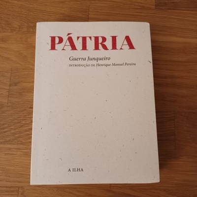 Livro 'PÁTRIA' de Guerra Junqueiro com capa branca e texto vermelho e preto, sobre superfície de madeira.